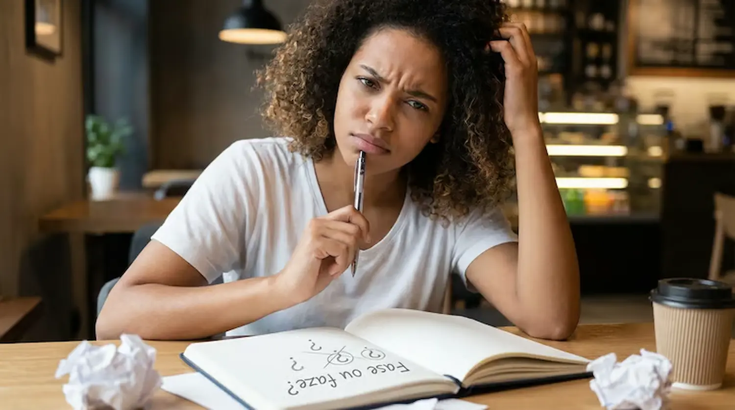 Mulher com expressão pensativa diante de um caderno com dúvida sobre o uso correto de fase ou faze.
