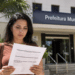 Mulher lê documento de concurso público em frente a uma prefeitura municipal.