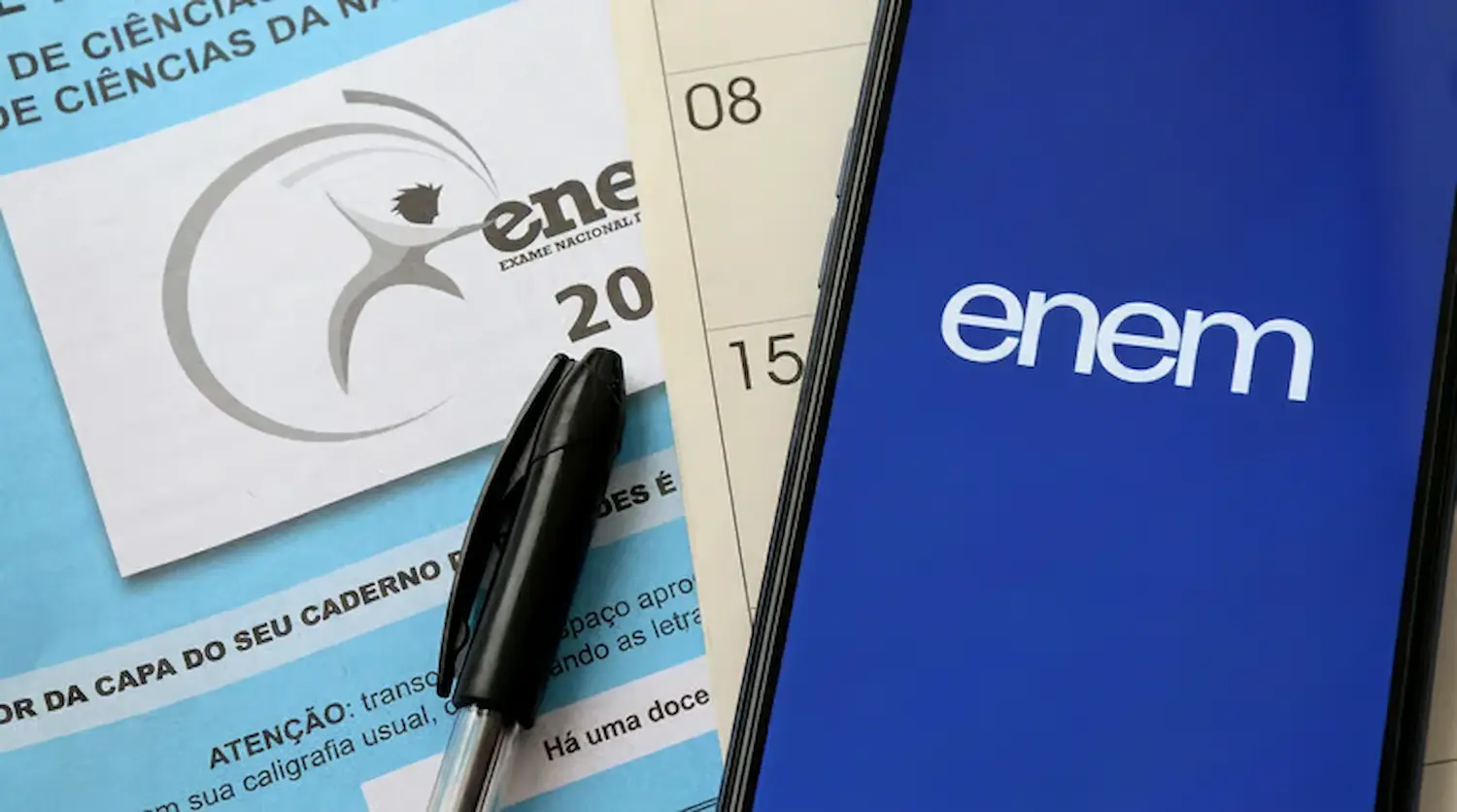 Cartão e caderno do Enem 2026 com caneta e celular mostrando a Página do Participante.