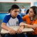 Estudante uniformizado recebe apoio de profissional em sala de aula durante atividade escolar