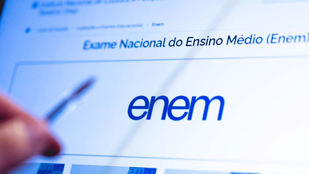 Logotipo do Enem exibido em tela de computador com mão segurando caneta.