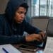 Jovem concentrado digitando no laptop, com expressão de preocupação, representando os golpes digitais durante o processo de inscrição no Enem 2026.