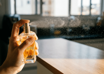 Mão borrifa perfume de frasco dourado sobre bancada de cozinha