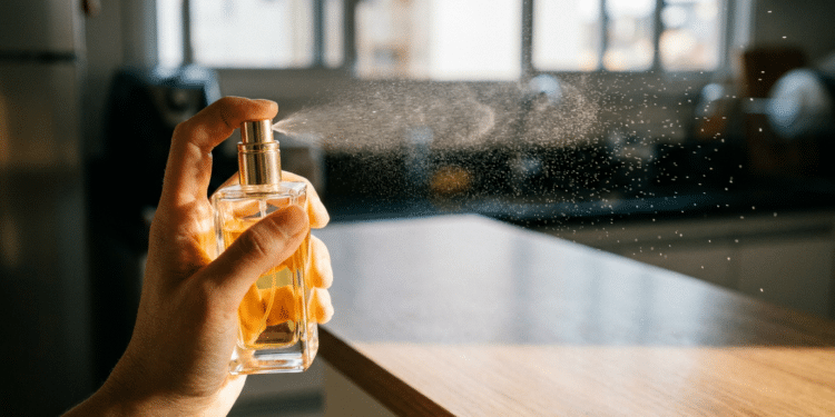 Mão borrifa perfume de frasco dourado sobre bancada de cozinha