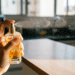 Mão borrifa perfume de frasco dourado sobre bancada de cozinha