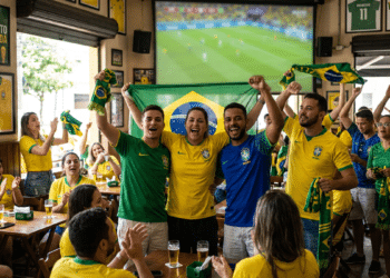 Torcedores vibram com a bandeira do Brasil diante de um telão durante jogo da Seleção em um bar