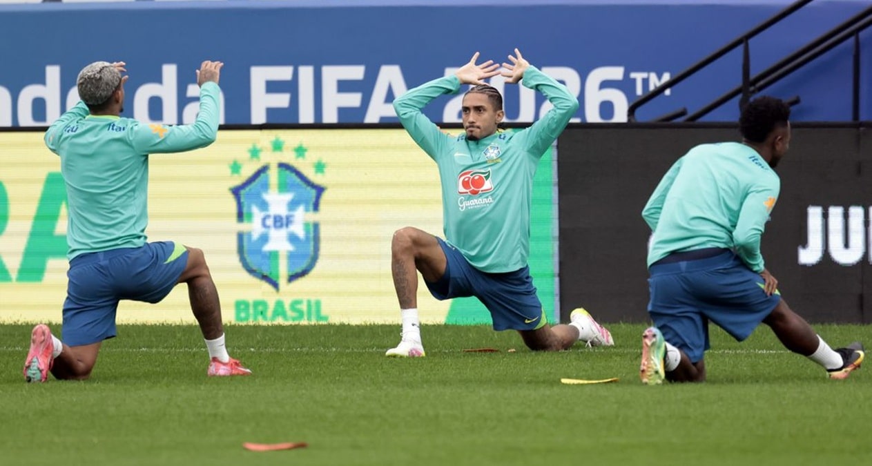 Jogadores da seleção brasileira fazem alongamento em treino diante de painel da Copa do Mundo FIFA 2026