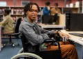 Estudante com deficiência em universidade utilizando computador em ambiente acessível e inclusivo.