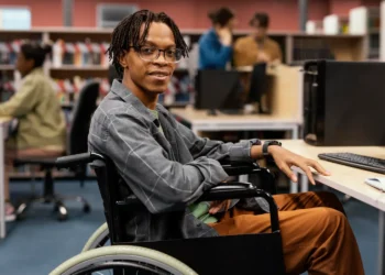 Estudante com deficiência em universidade utilizando computador em ambiente acessível e inclusivo.