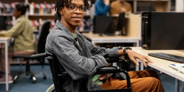 Estudante com deficiência em universidade utilizando computador em ambiente acessível e inclusivo.