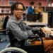 Estudante com deficiência em universidade utilizando computador em ambiente acessível e inclusivo.