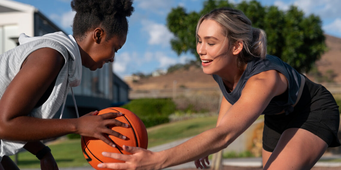 Duas jovens disputam uma bola de basquete em quadra ao ar livre