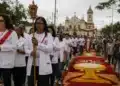 iéis participando de uma procissão de Corpus Christi em rua brasileira, com tapetes coloridos de serragem e flores, representando o feriado de Corpus Christi.