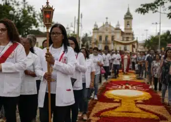 iéis participando de uma procissão de Corpus Christi em rua brasileira, com tapetes coloridos de serragem e flores, representando o feriado de Corpus Christi.