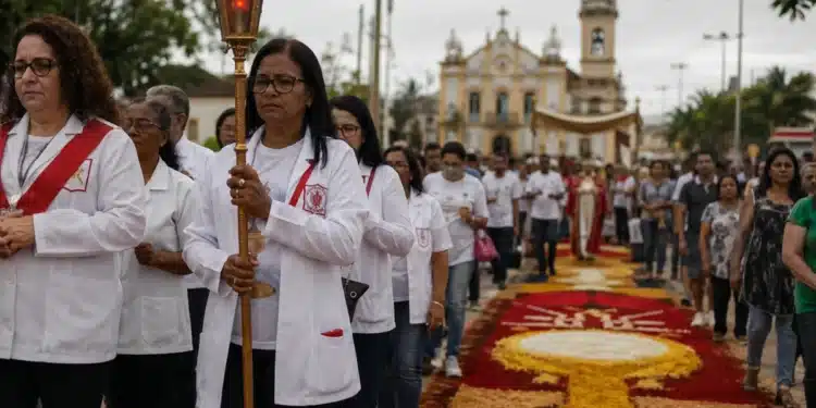 iéis participando de uma procissão de Corpus Christi em rua brasileira, com tapetes coloridos de serragem e flores, representando o feriado de Corpus Christi.