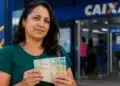 Mulher segurando cédulas de dinheiro em frente a uma agência da Caixa, simbolizando a liberação do FGTS no valor de R$ 900 disponível até 30 de junho