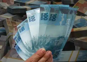 Mão segurando notas de real, simbolizando o saque de R$ 6.220 disponível para solicitação por meio do aplicativo FGTS.