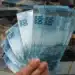 Mão segurando notas de real, simbolizando o saque de R$ 6.220 disponível para solicitação por meio do aplicativo FGTS.