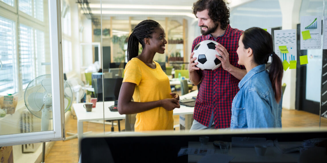 Colegas de trabalho conversam segurando uma bola de futebol em um escritório