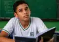 Estudante brasileiro com caderno em sala de aula pública, representando regra de frequência para recebimento do benefício mensal do Pé-de-Meia.