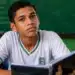 Estudante brasileiro com caderno em sala de aula pública, representando regra de frequência para recebimento do benefício mensal do Pé-de-Meia.