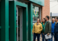 Grupo de pessoas em frente à porta de uma agência bancária, com bandeiras do Brasil na rua