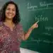 Professora brasileira apontando para o quadro com a palavra “hífen” em sala de aula