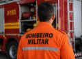 Bombeiro militar visto de costas em frente a viatura do Corpo de Bombeiros durante operação.