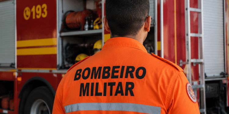 Bombeiro militar visto de costas em frente a viatura do Corpo de Bombeiros durante operação.