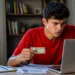 Jovem estudante brasileiro de 18 anos segurando o RG, concentrado no laptop, representando a inscrição no Enem 2026.