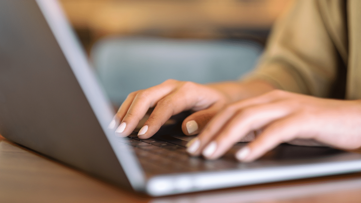 Mãos de mulher com unhas pintadas digitação notebook prata foco mãos.