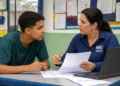Estudante recebe orientação sobre inscrições do Sisu+ 2026 em ambiente escolar, com papéis e notebook sobre a mesa.