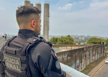 Agente da Polícia Penal de costas observa muro de unidade prisional