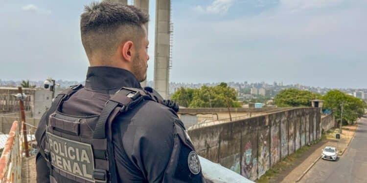 Agente da Polícia Penal de costas observa muro de unidade prisional