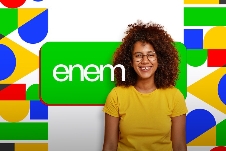 Jovem de cabelo cacheado e óculos, usando camiseta amarela, sorri em frente ao logotipo verde do Enem.