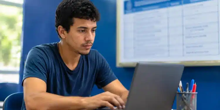Jovem brasileiro utilizando um notebook, representando o período de inscrição prorrogado até 10 de julho.