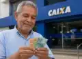 Aposentado brasileiro segurando dinheiro em frente à agência da Caixa Econômica Federal, representando o início dos pagamentos do INSS em 24 de junho.