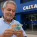 Aposentado brasileiro segurando dinheiro em frente à agência da Caixa Econômica Federal, representando o início dos pagamentos do INSS em 24 de junho.