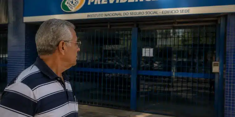 Idoso observando agência do INSS fechada, representando a suspensão de pagamentos de benefícios nesta quinta-feira, 4 de junho.