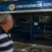 Idoso observando agência do INSS fechada, representando a suspensão de pagamentos de benefícios nesta quinta-feira, 4 de junho.