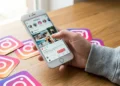 Pessoa usando o Instagram em um celular sobre uma mesa com ícones da rede social, em contexto de debate sobre localização em tempo real e proteção de dados.