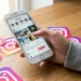 Pessoa usando o Instagram em um celular sobre uma mesa com ícones da rede social, em contexto de debate sobre localização em tempo real e proteção de dados.