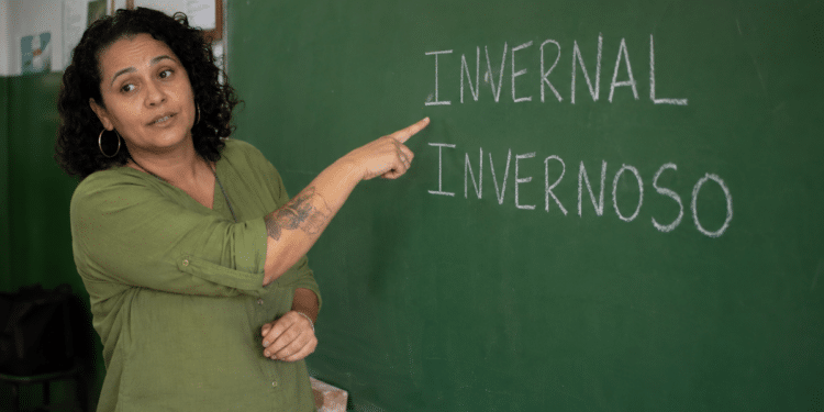 Professora em sala de aula apontando para lousa com as palavras invernal e invernoso escritas em giz.