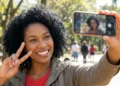 Mulher sorrindo fazendo selfie com iPhone em parque ao ar livre.