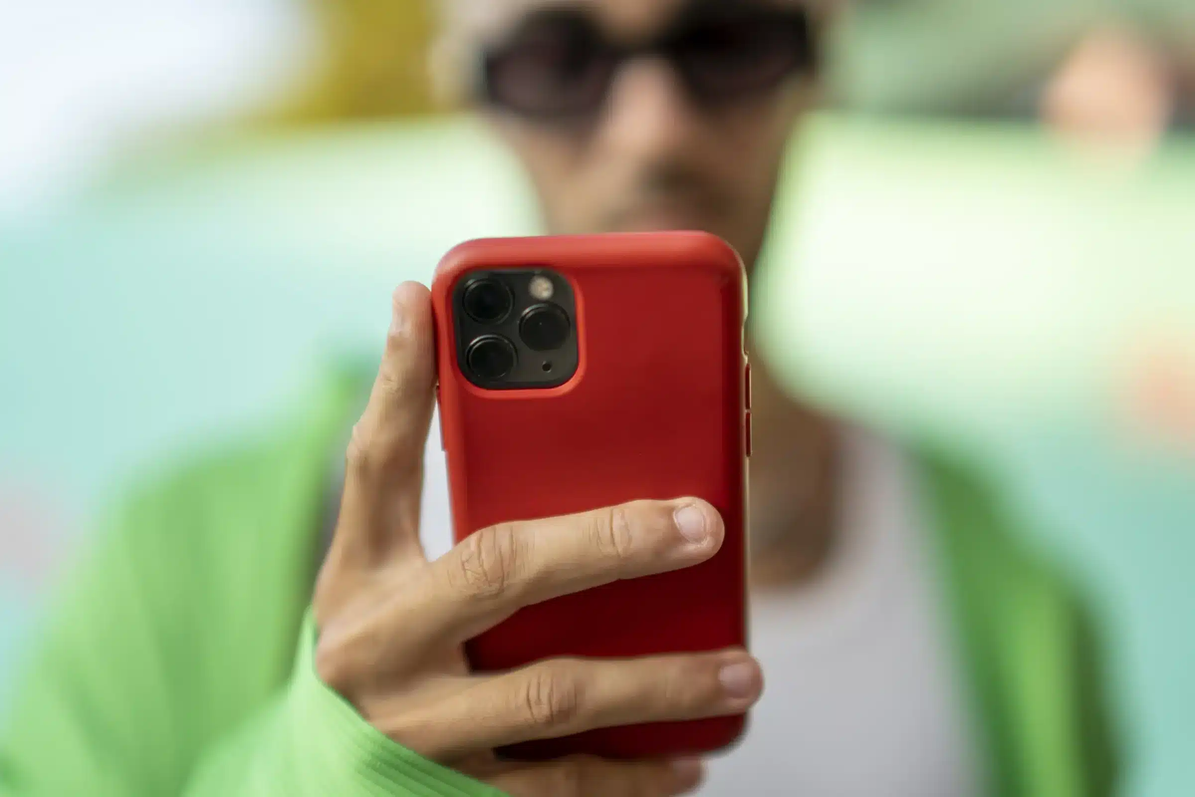 iPhone Pessoa segurando smartphone vermelho em destaque, representando medidas do Cade contra a Apple e possíveis sanções por descumprimento de acordo regulatório.