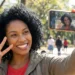 Mulher sorrindo fazendo selfie com iPhone em parque ao ar livre.