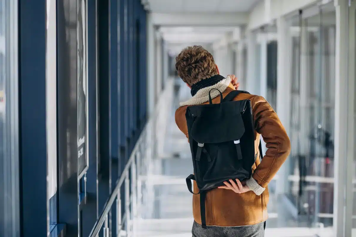 Estudante caminhando em corredor universitário com mochila, representando rotina acadêmica em dia de aulas durante jogos do Brasil na Copa
