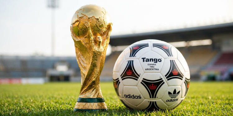 Taça da Copa do Mundo ao lado de uma bola de futebol no gramado