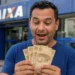 Brasileiro segurando notas de real em frente a uma agência da Caixa, representando a liberação de saque de R$ 6.220.