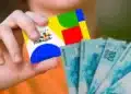 Mão segurando cartão do Bolsa Família com notas de reais ao fundo, ilustrando o pagamento do benefício conforme o NIS nesta quarta-feira (24).